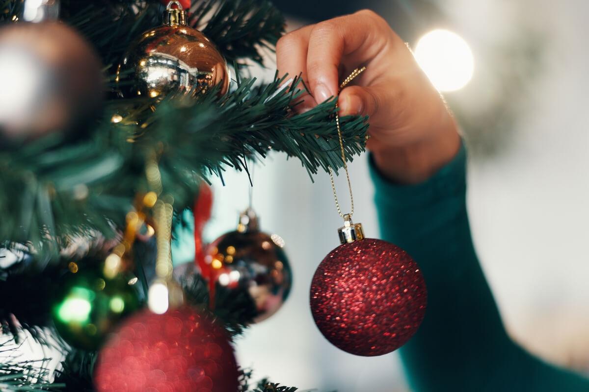 Person hangs ornament on Christmas tree.