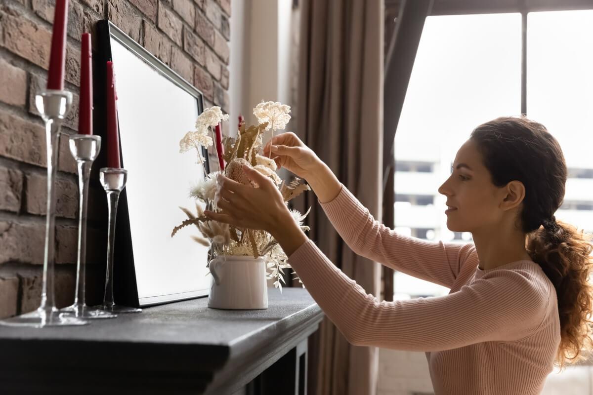 Woman fixes flowers in vase on her fireplace mantle.