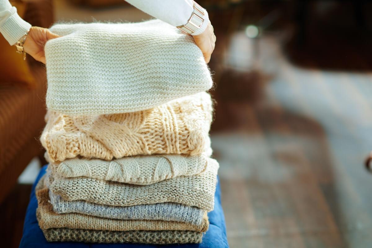 Hands placing sweater on top of pile of sweaters.