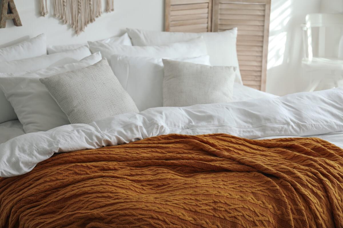 Bed with tons of pillows, white comforter, and orange quilt on it.
