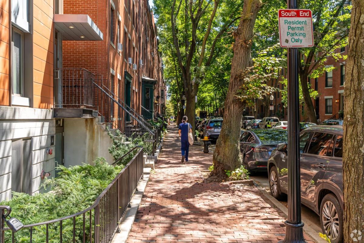 Person walking on sidewalk in Boston past parked cars and parking sign.