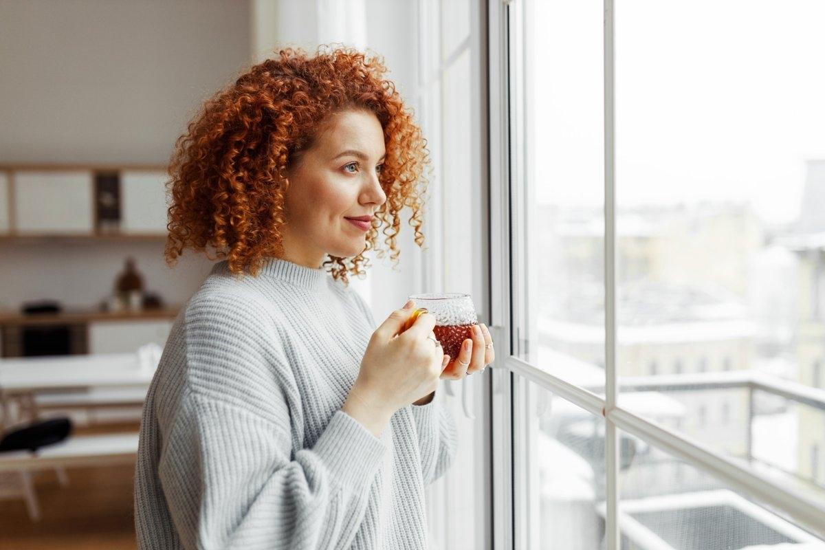 A lady gazing out her window with a cup of hot tea.