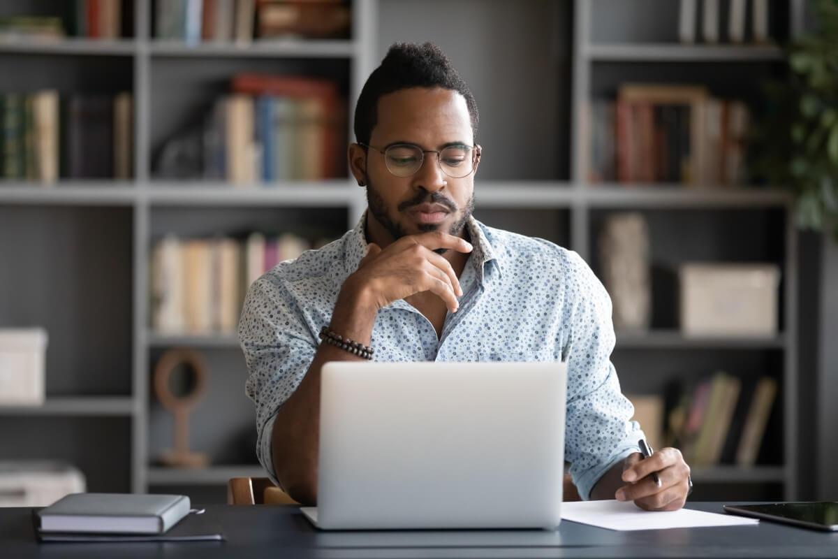 Man taking notes while reading off laptop.