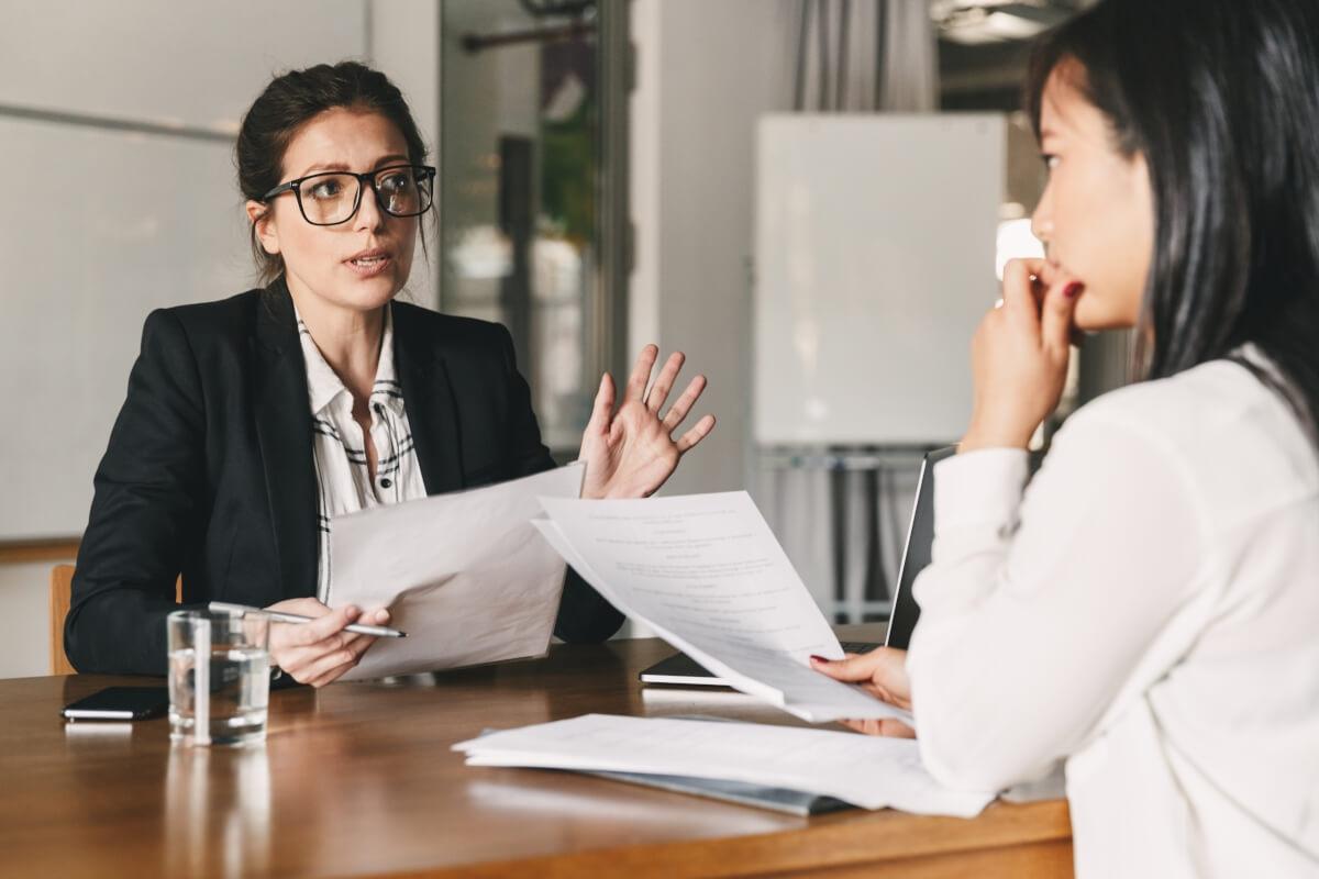 Two women sitting across from each other at desk having a serious discussion