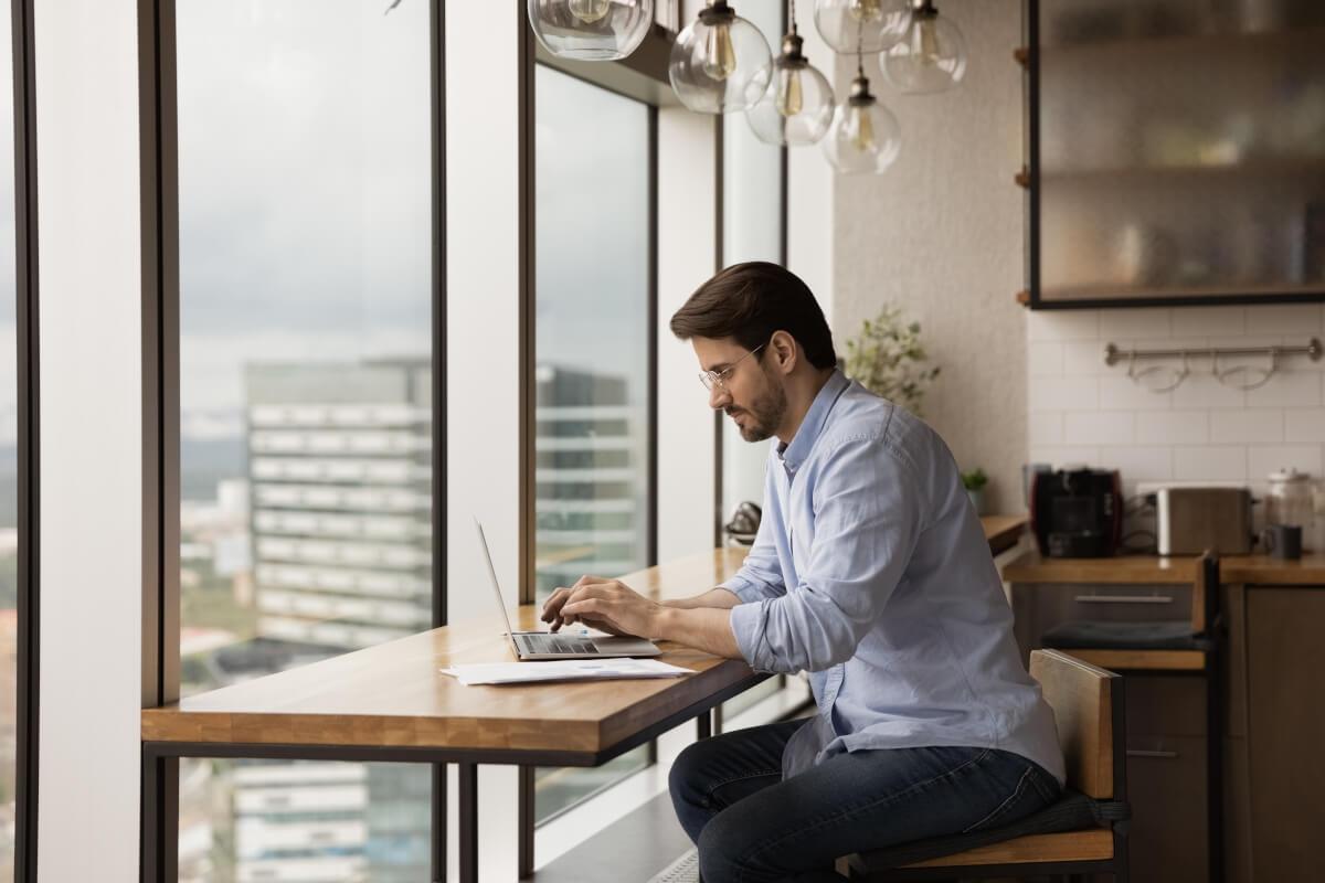Man with glasses typing on his laptop in a high-rise apartment.