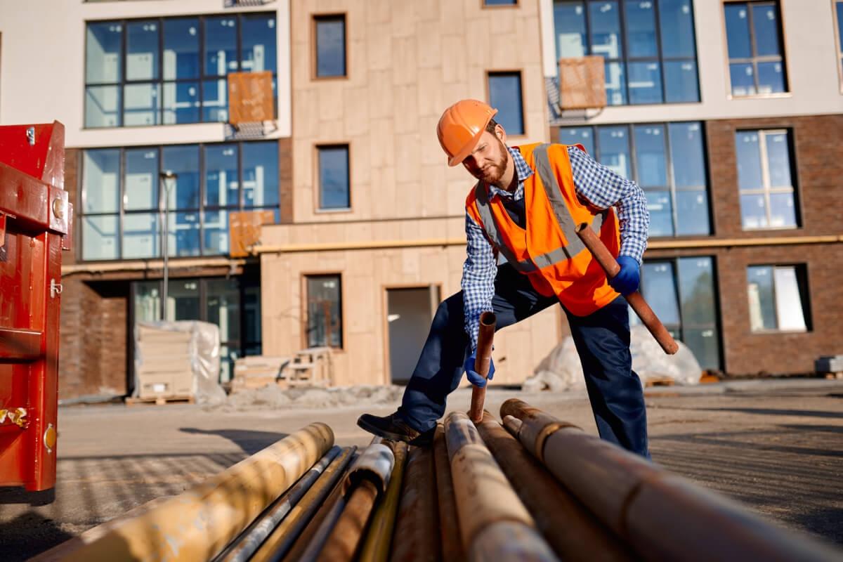 Construction worker holding a pipe in front of apartment building that is under construction.