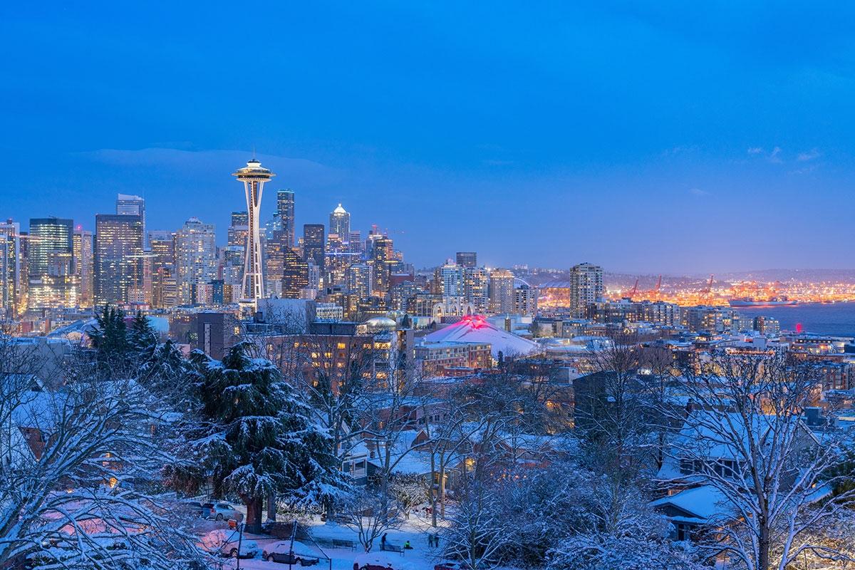 Seattle's skyline glows with lights during the evening as everything is covered with snow.