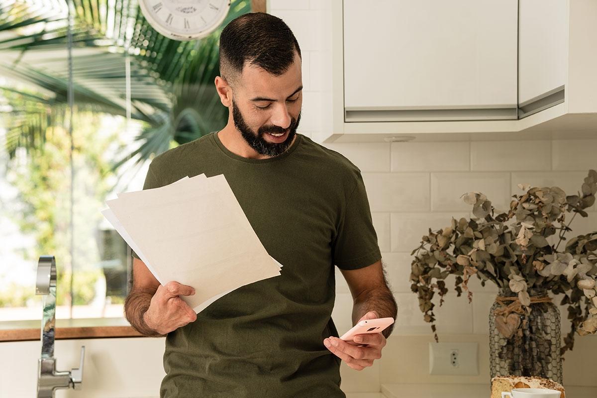Man checking his phone while holding papers.