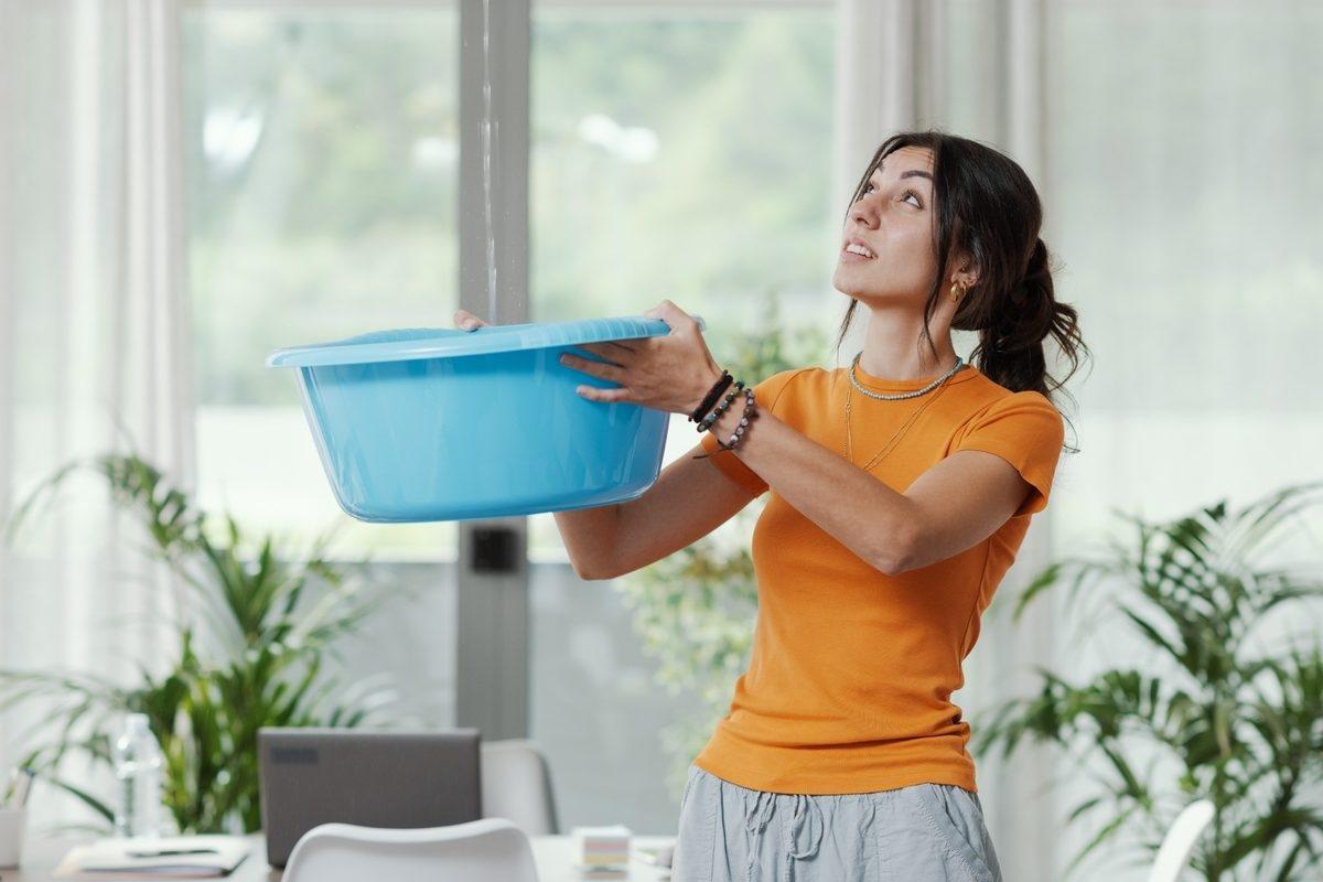 A renter holding a bucket to catch water from the ceiling