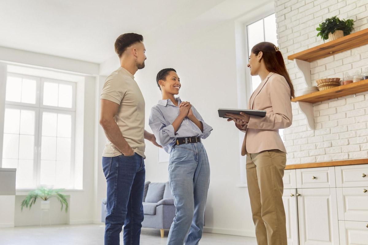 A young couple smiles while touring an apartment with exposed brick.