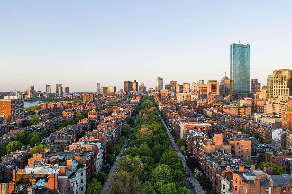The rowhouses surrounding the Commonwealth Avenue Mall stretch out during sunset with skyscrapers of downtown in the background.