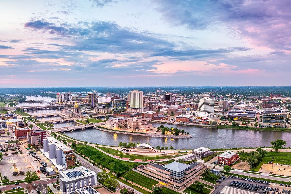 The Cedar River winds through Cedar Rapids, multiple bridges crossing the water, and office buildings and neighborhoods on both sides under a cloudy evening sky.