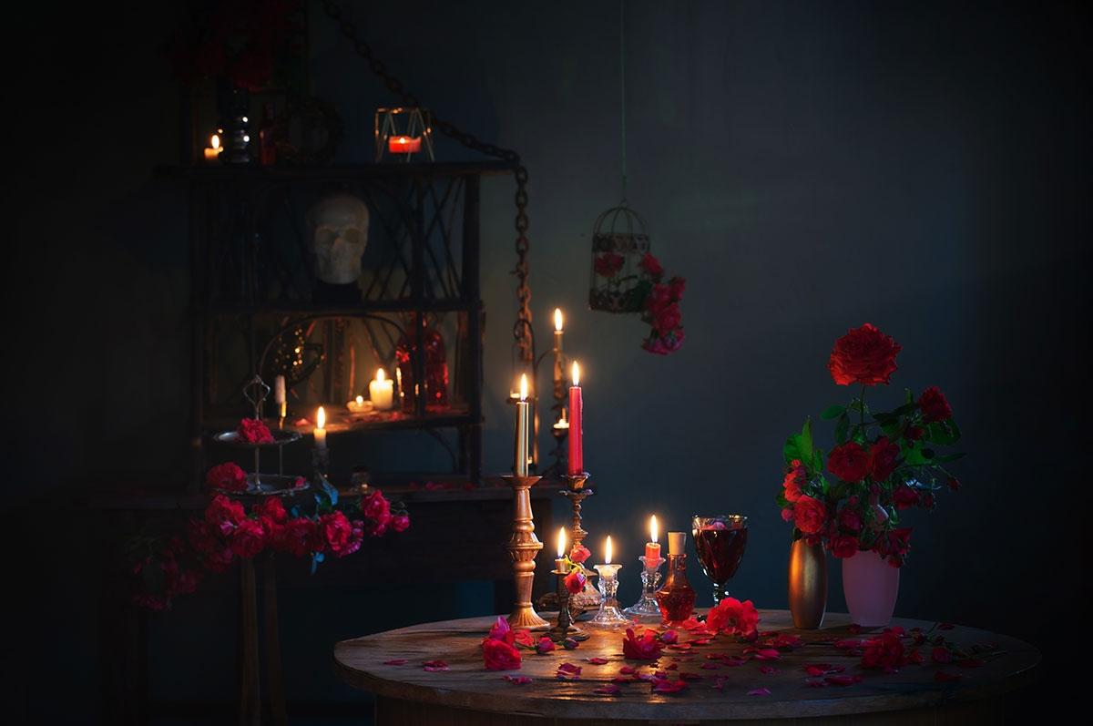 A candlelit table arranged with red roses, glassware, and decorative objects creates an intimate, dramatic atmosphere.