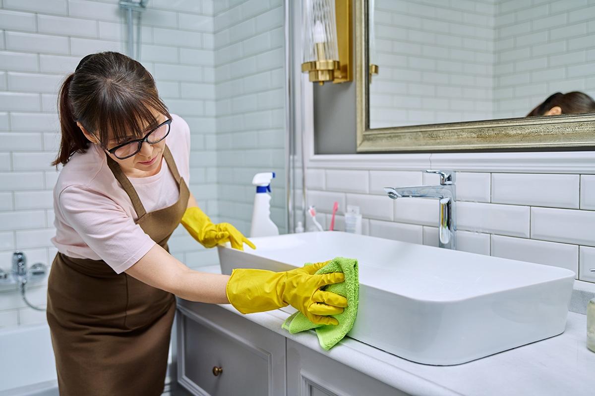 Woman in protective gear cleaning the outside of a bathroom sink.