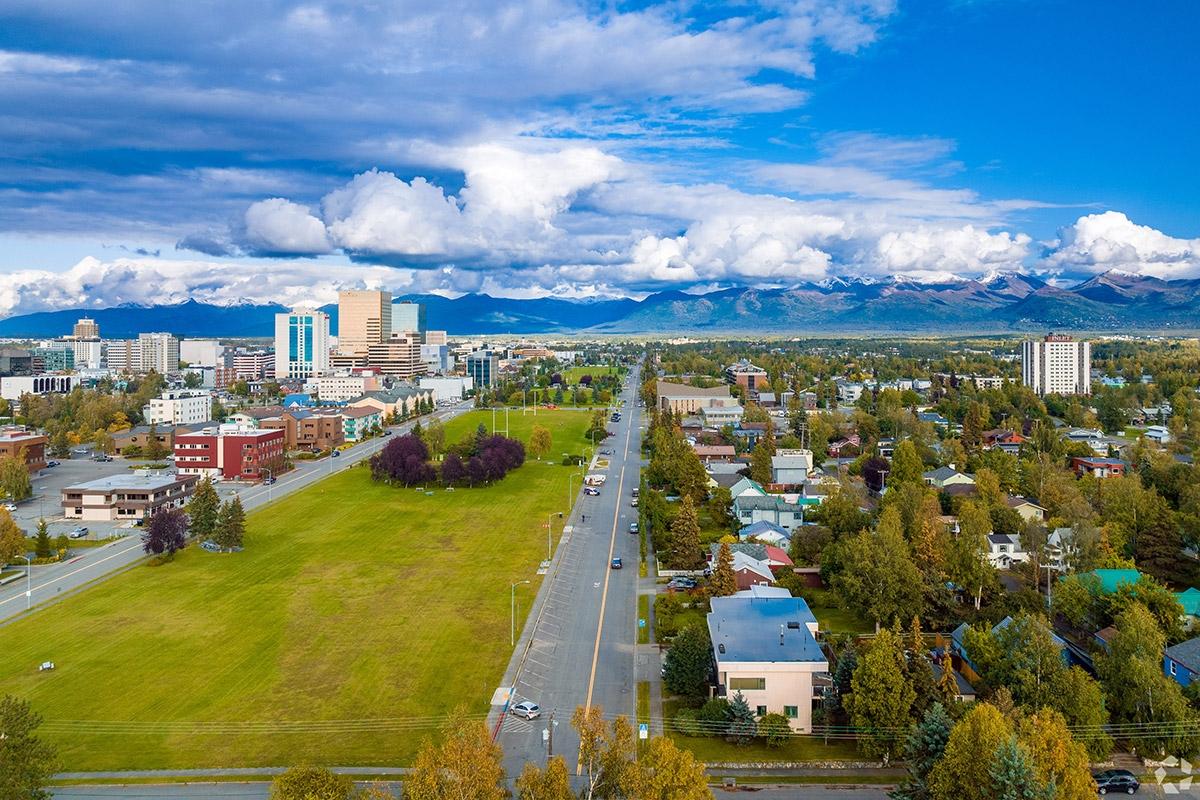 High-rises in Downtown Anchorage rise next to tree-filled neighborhoods with a road seperating them.
