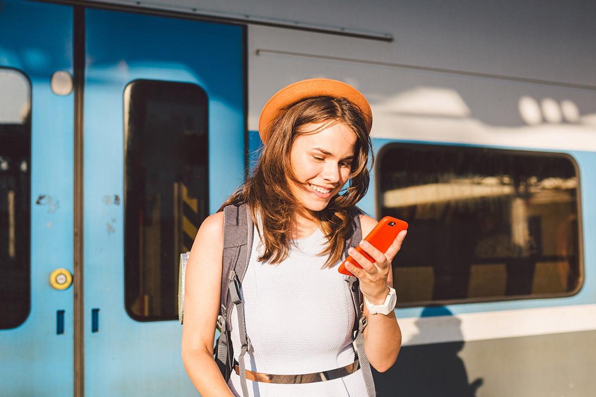 Woman on phone in front of train while smiling.