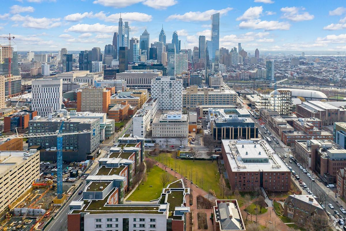 Campus buildings and a courtyard sit on busy streets with Downtown Philadelphia in the distance.
