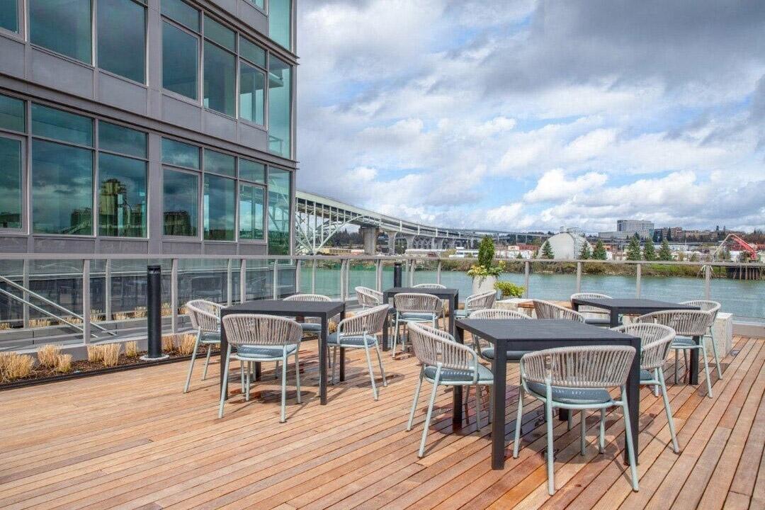 An outdoor deck with chairs and tables sits right next to the river in a luxury apartment community in Portland.