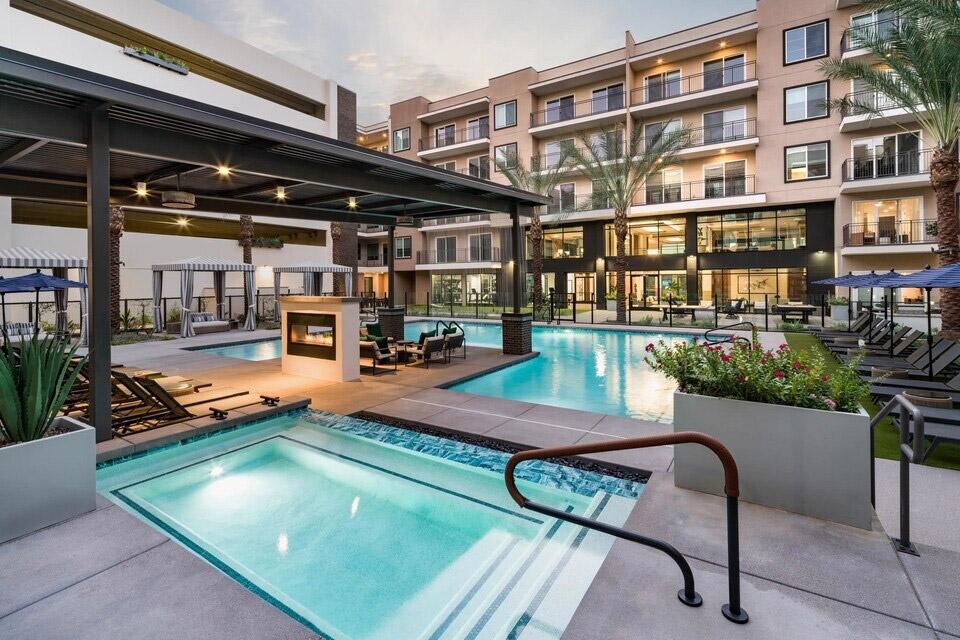 A resort-style pool is surrounded by lounge chairs and cabanas in a luxury apartment community.