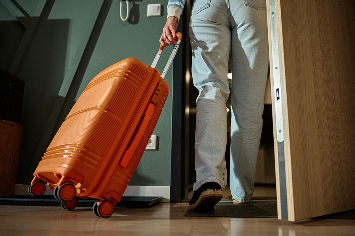 A renter walking out of their pied-a-terre with luggage.