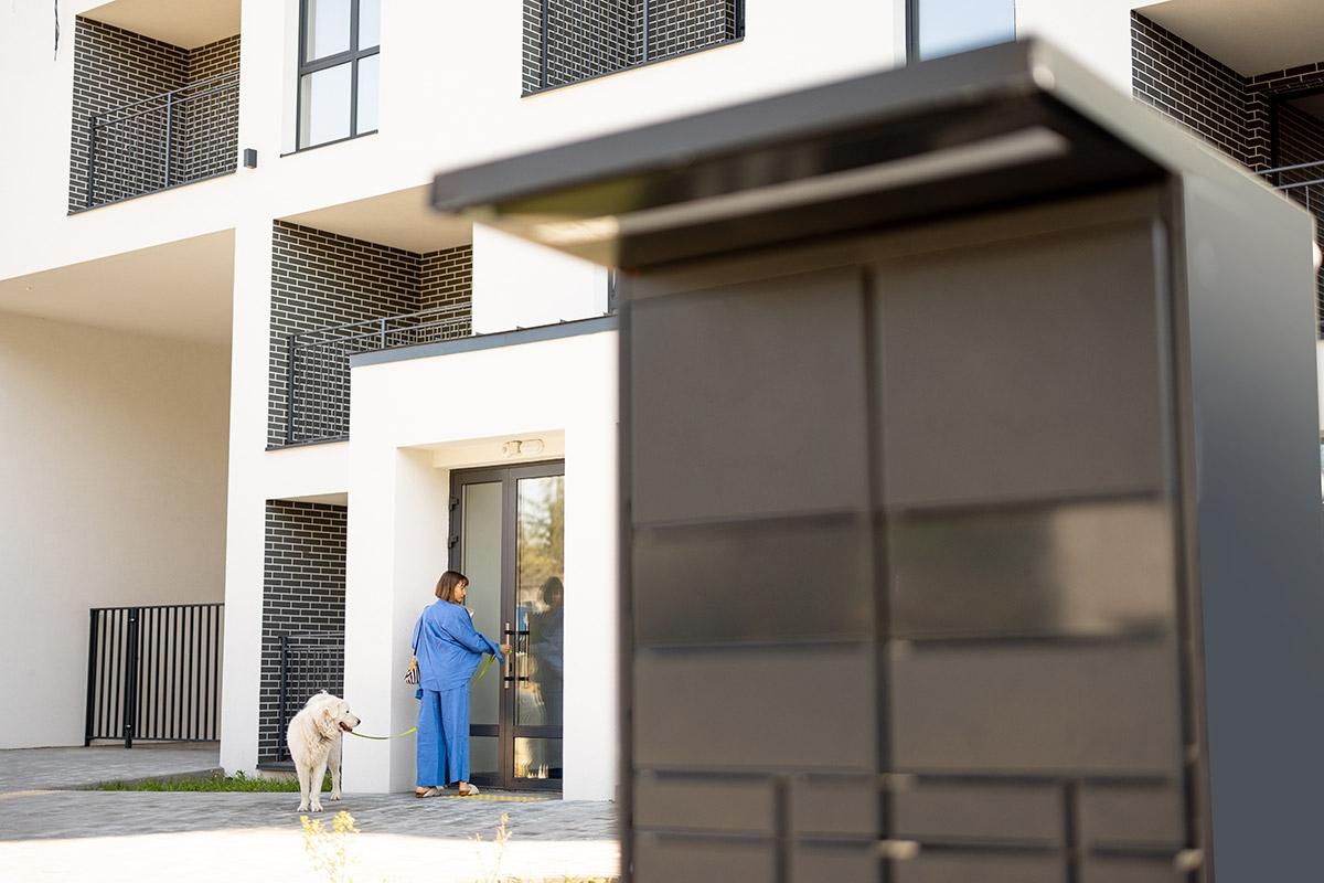 A woman with a dog entering a controlled-access apartment building with mailboxes in the front.