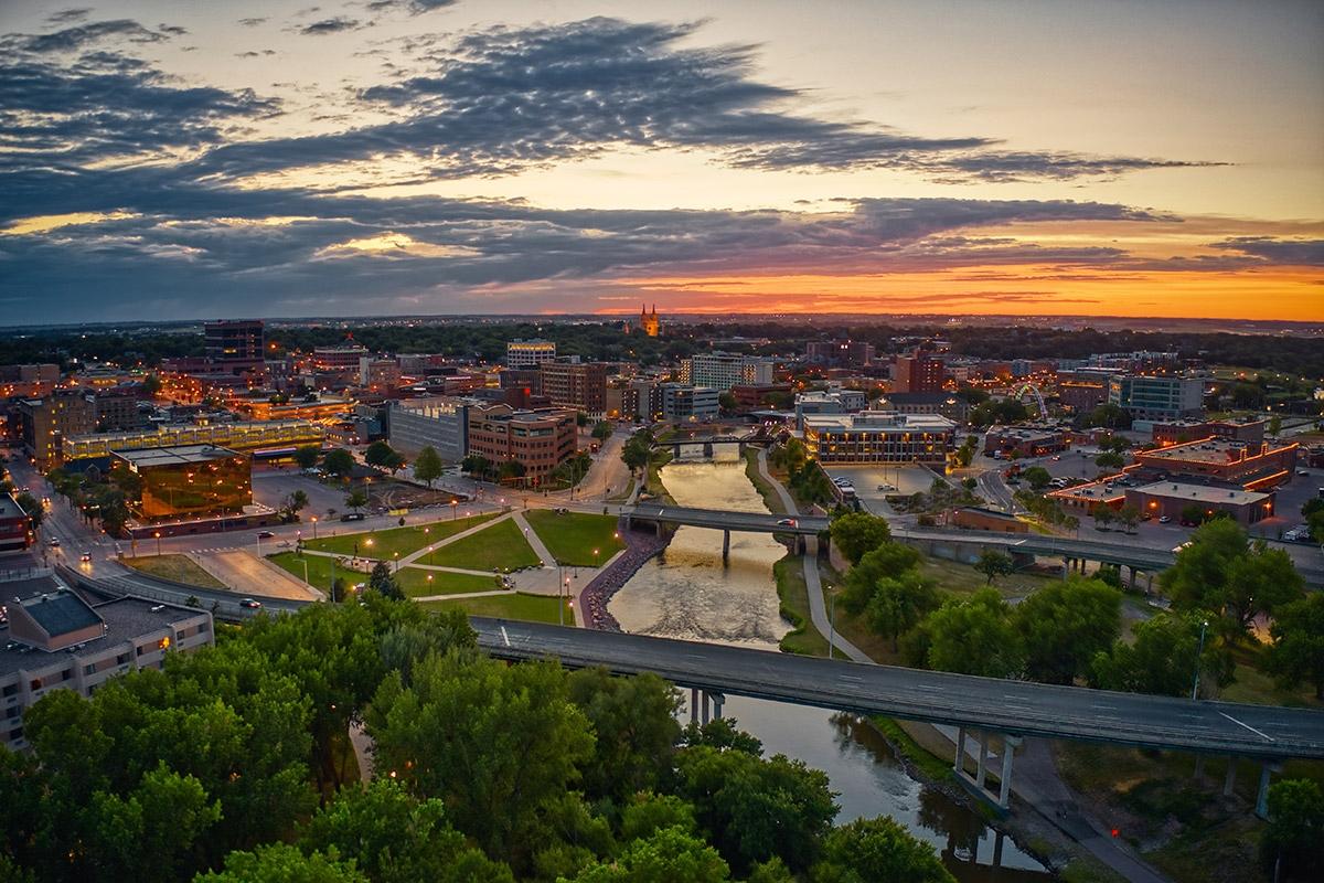 Buildings glow with light as the sun set over Sioux Falls with the river in the middle.