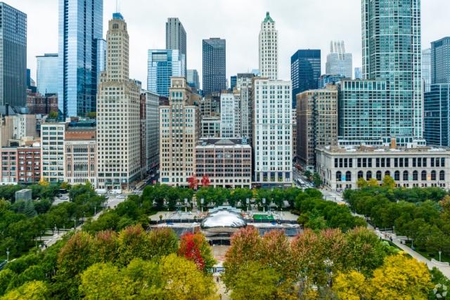 An aerial view of Millennium Park in Chicago shows The Bean sculpture in front of the Chicago skyline.