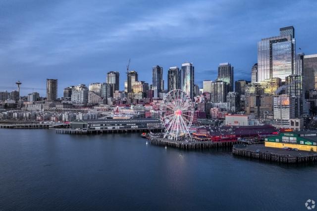The Seattle Great Wheel sits on the pier as the Seattle skyline rises behind it.