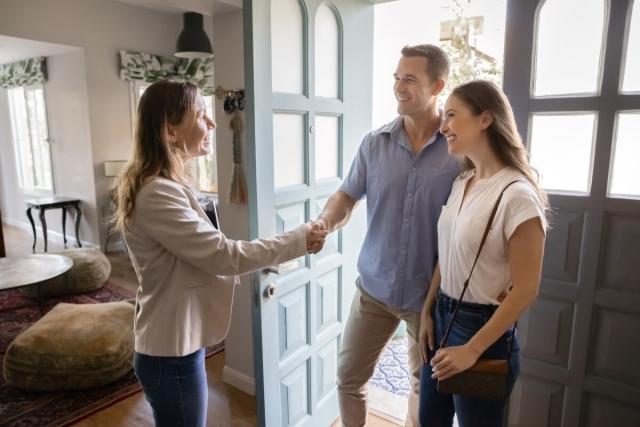 A private landlord shakes the hands of a young couple as she welcomes them into a rental.