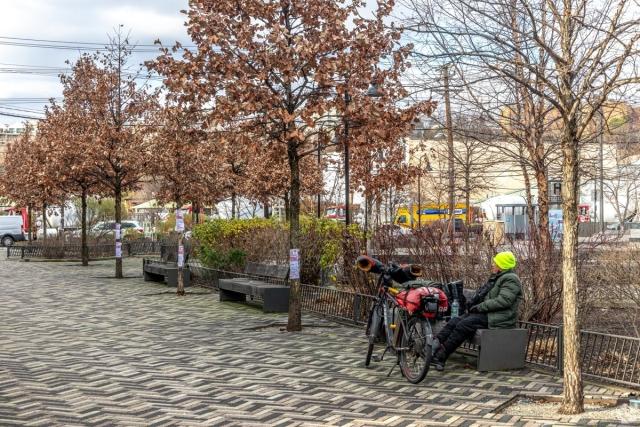 Quiet Hoboken park with patterned stone walkway, trees, and cyclist resting – relaxing, budget-conscious vibe near Western Edge.