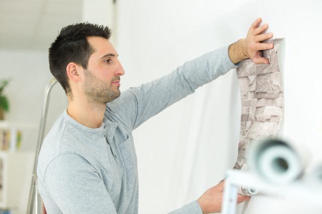Tenant puts up wallpaper in his apartment.