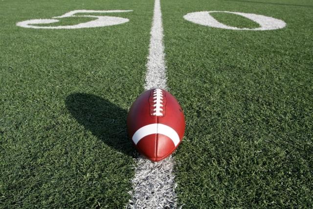 A football resting on the 50 yard line on football field