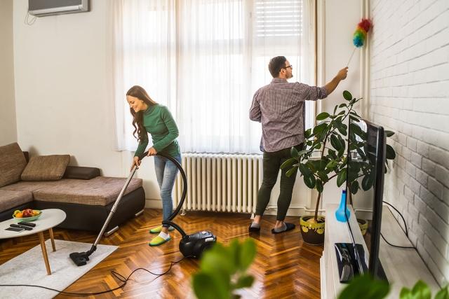 Woman vacuums while man dusts as they clean their apartment.