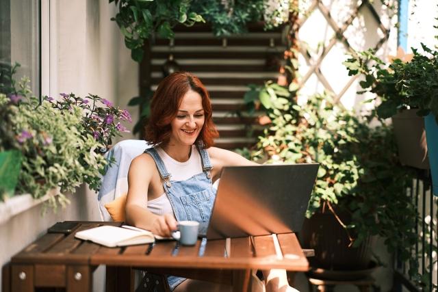 Woman on laptop on cozy balcony covered with plants.