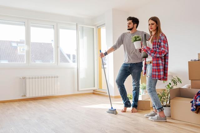 Couple of a man and woman cleaning empty apartment with moving boxes behind them.