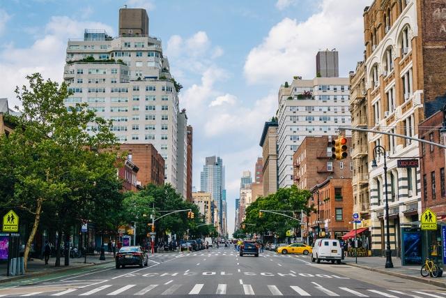 The tree-covered streets of New York are lined with tall buildings, people, and cars.