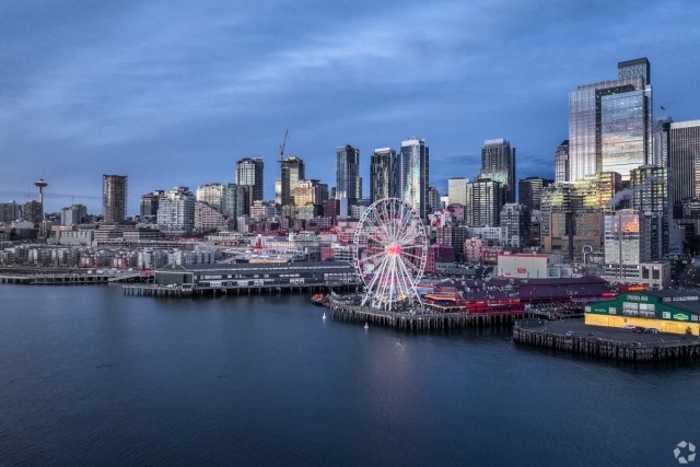 The Seattle Great Wheel sits on the pier as the Seattle skyline rises behind it.