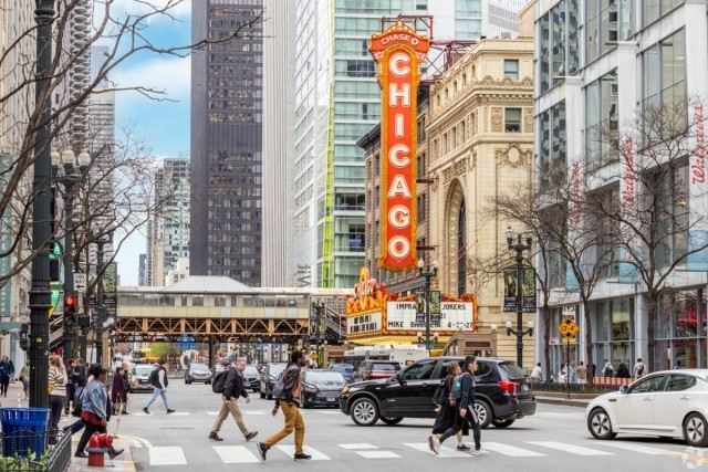 Busy downtown Chicago street with pedestrians crossing in front of the iconic Chicago Theatre sign and elevated train tracks