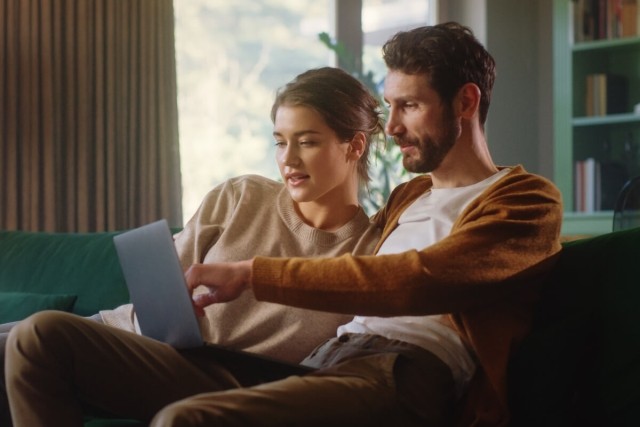 Man and woman sitting on couch and looking at laptop together.