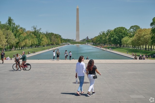 People walk in front of the Reflecting Pool with the Washington Monument in the background.
