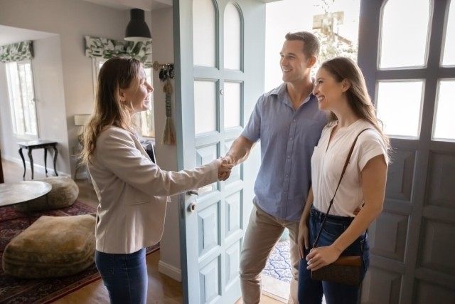A private landlord shakes the hands of a young couple as she welcomes them into a rental.