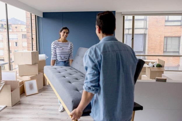 A couple carries a couch into their new apartment.