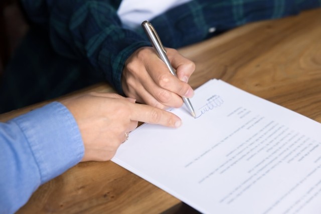 A landlord points to the line where a tenant signs their name on a lease agreement.