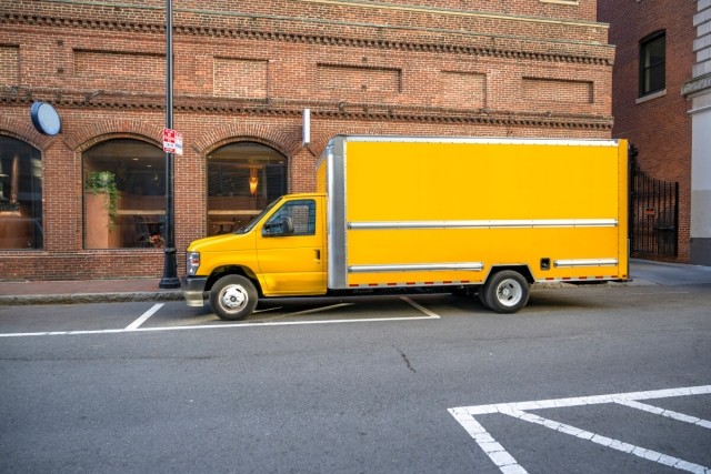 A yellow box truck is parked outside a brick building in Boston.