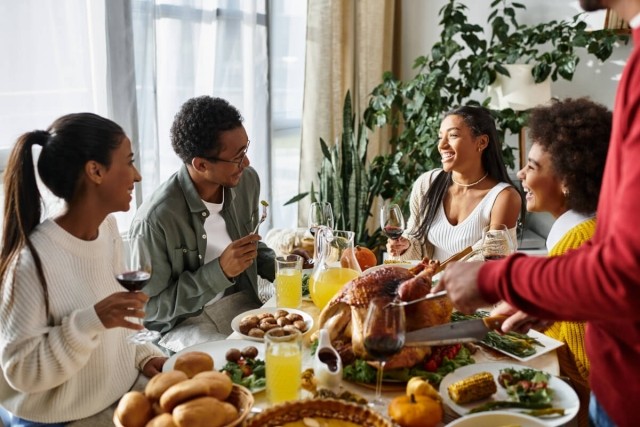 Friends laughing around a table filled with traditional Thanksgiving foods.