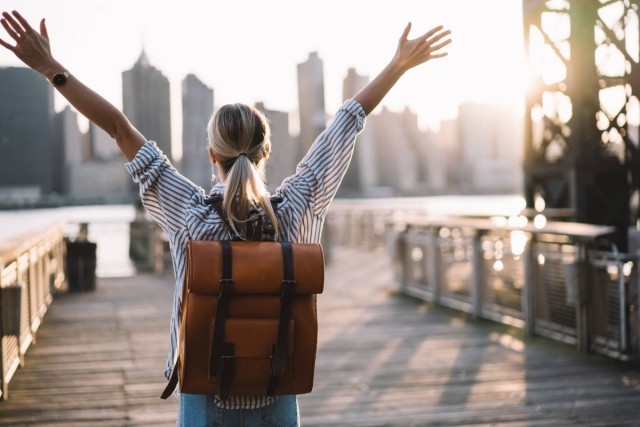 Woman holds hands up and watches a city skyline.