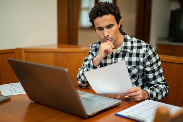 Man looking over papers and laptop.