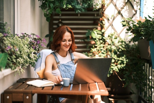 Woman on laptop on cozy balcony covered with plants.