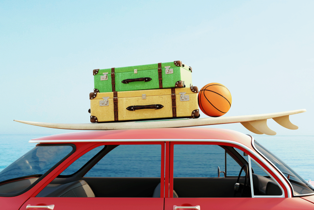 A red car with a surfboard, luggage, and a basketball on its roof