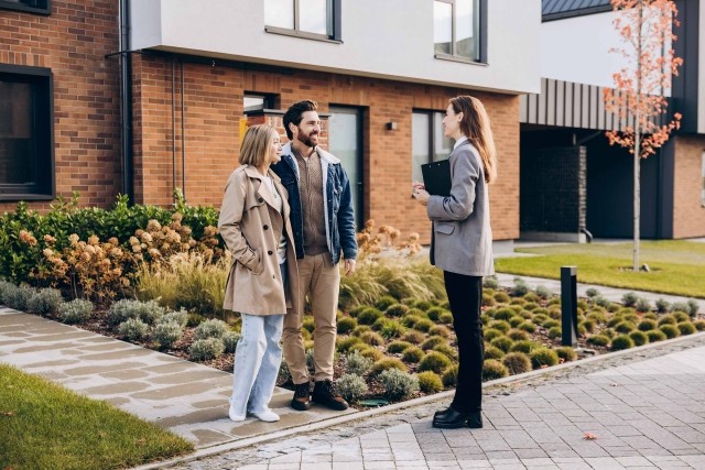 Couple standing with a rental agent outside of an apartment building.